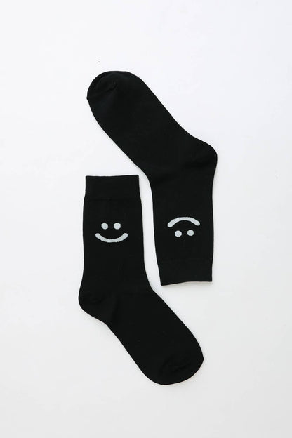 Pair of black crew socks with smiley and sad face design on white background
