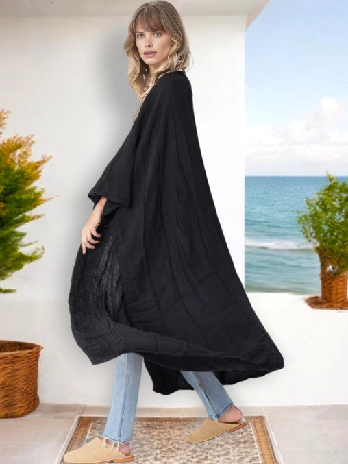 Woman wearing a flowing black kimono cardigan with jeans and flats, standing on a patio near the ocean