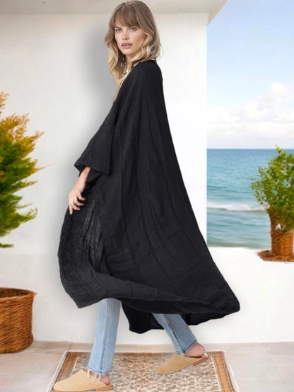 Woman wearing a flowing black kimono cardigan with jeans and flats, standing on a patio near the ocean