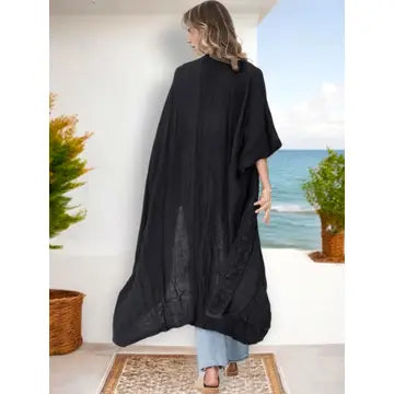 Woman wearing a long black open-front kimono, styled outdoors near the ocean.