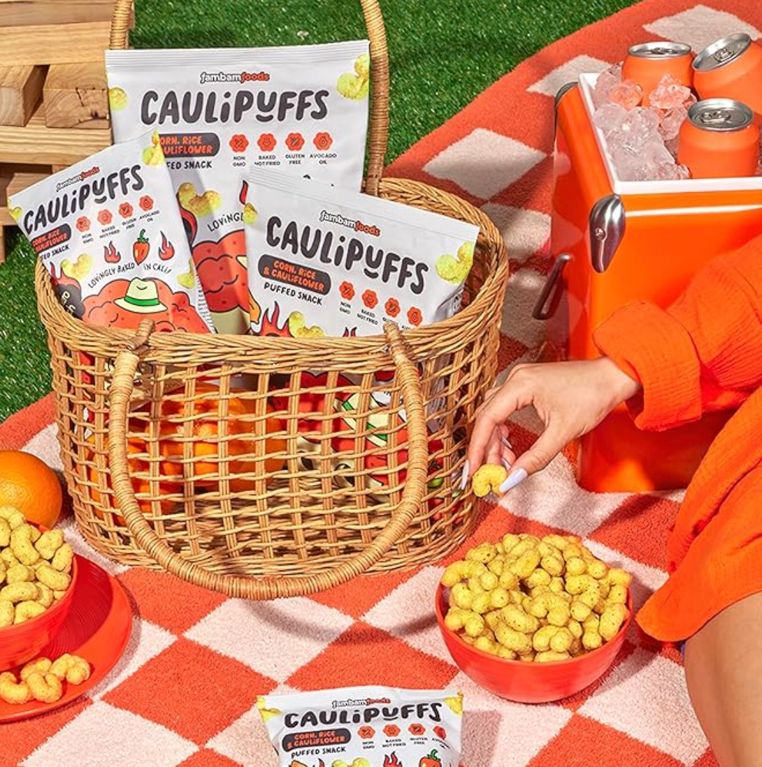 CauliPuffs Hot Habanero Ranch puffed snacks in a picnic basket with bowls of puffs, cooler, and blanket setup outdoors.