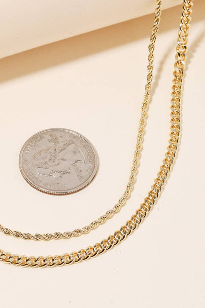 Two gold chain necklaces displayed on a beige surface with a silver coin for size comparison.
