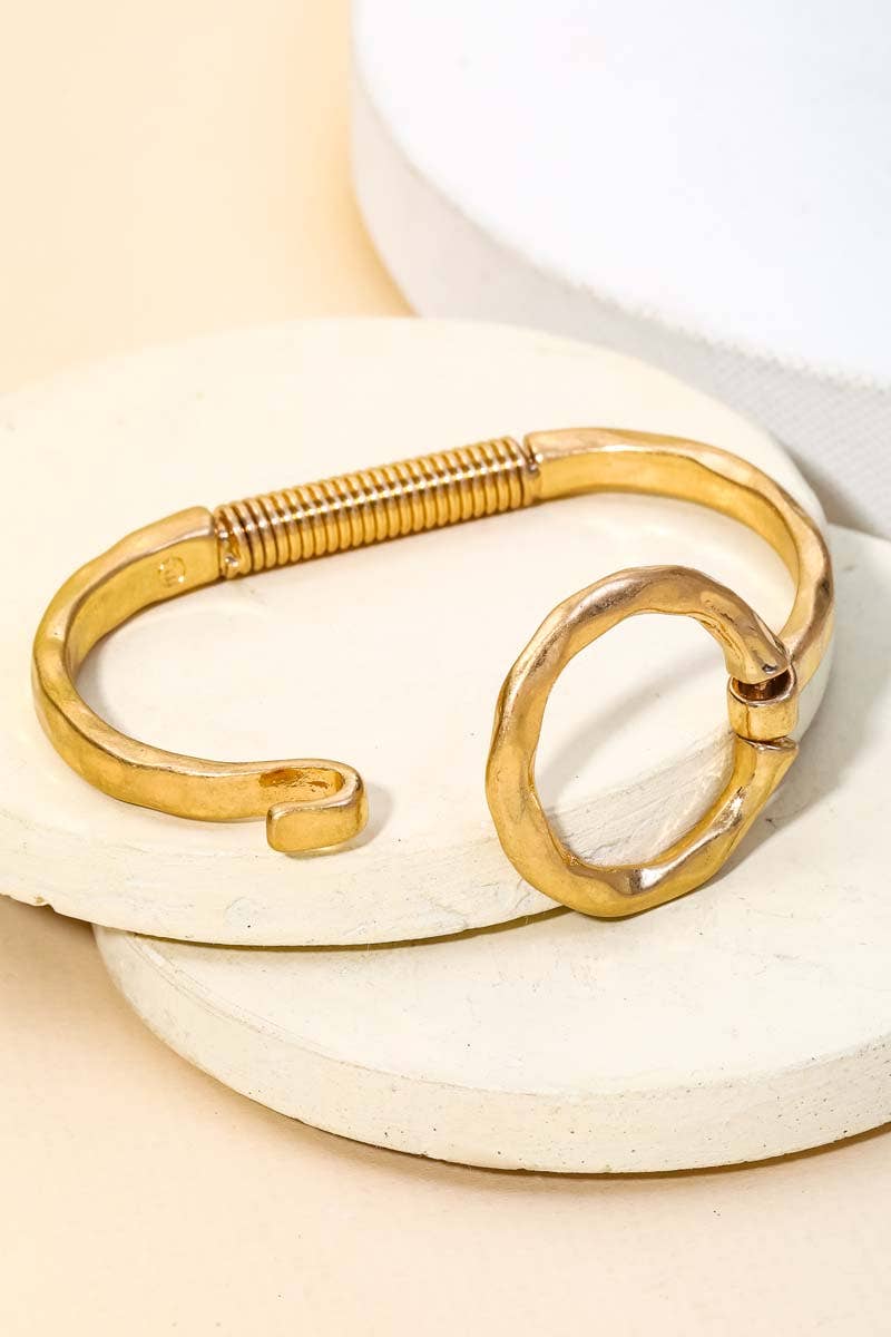 Gold circle bracelet displayed on stacked white stone surfaces with beige background.