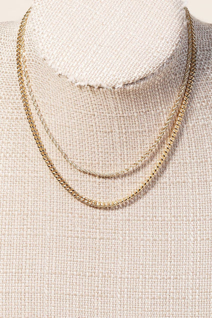 Gold layered chain necklace displayed on a beige mannequin bust