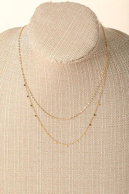 Delicate gold layered necklace displayed on a beige mannequin bust.