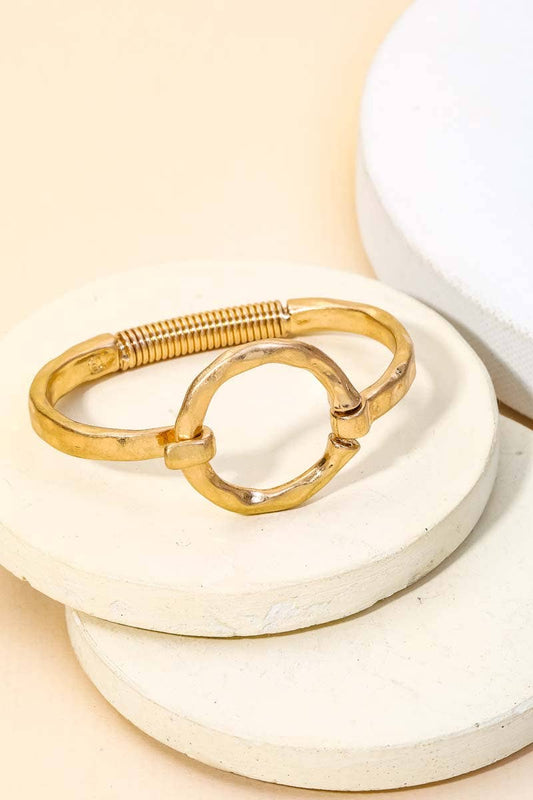 Gold open cuff bracelet displayed on stacked white stone surfaces with beige background.