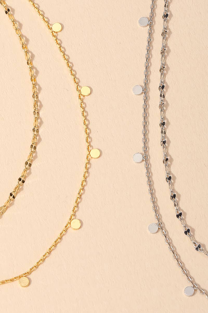 Gold and silver layered necklaces with delicate round pendants on a beige background.