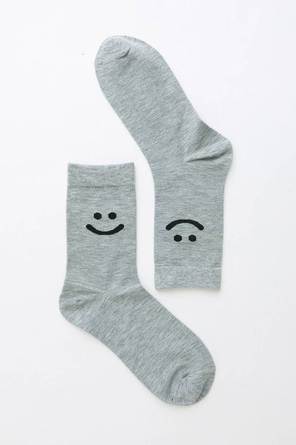 Pair of light gray crew socks with smiley and sad face design on white background