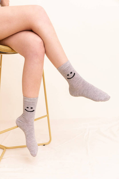 Person wearing gray crew socks with smiley face design, seated on chair