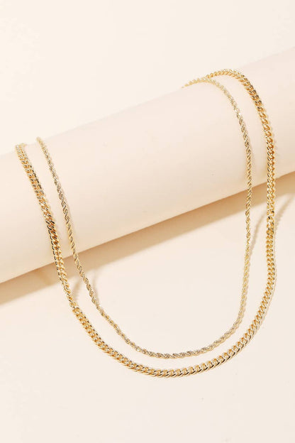 Two gold chain necklaces draped on a round beige display surface.