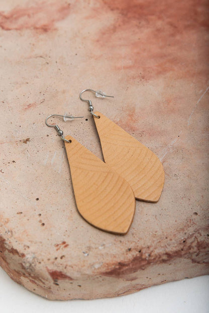 Leather teardrop earrings displayed on a textured stone surface.