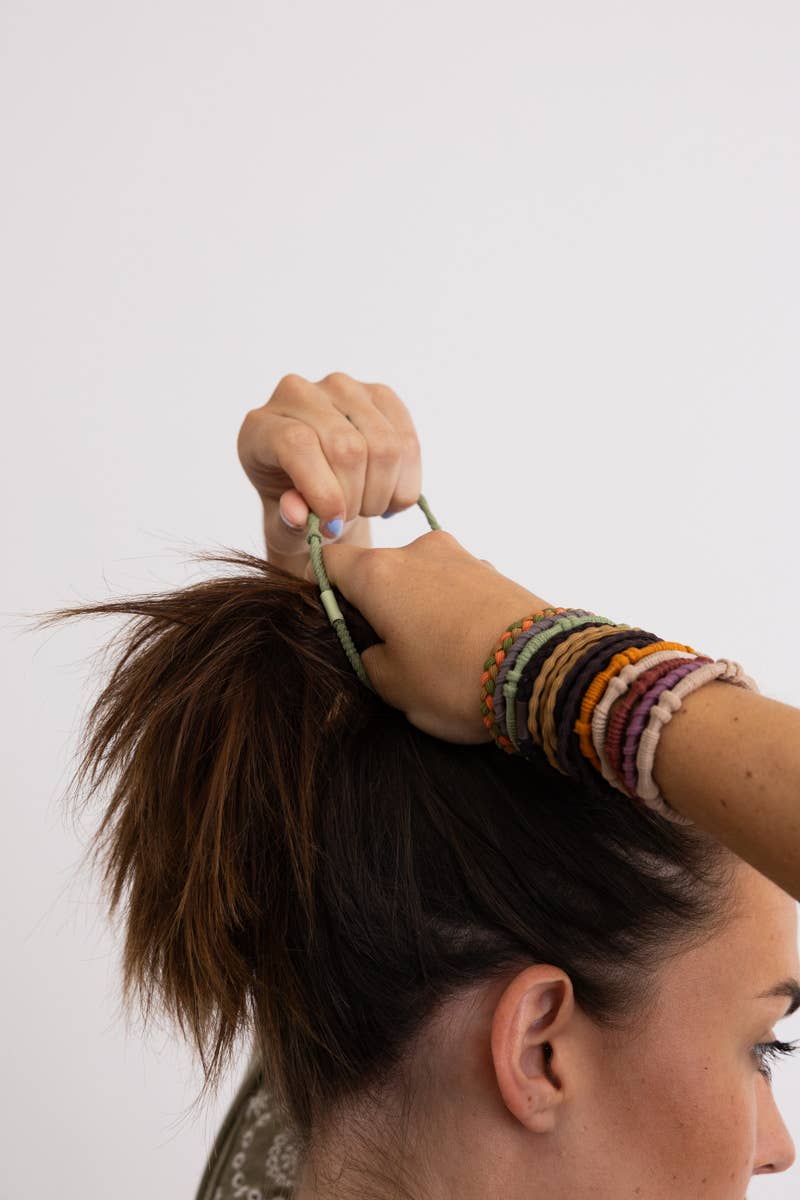 Person tying messy bun wearing colorful beaded bracelets