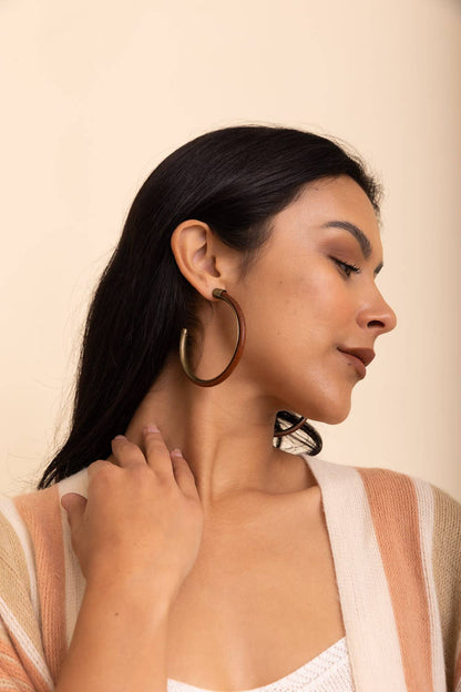Woman wearing large bronze hoop earrings against a beige background.