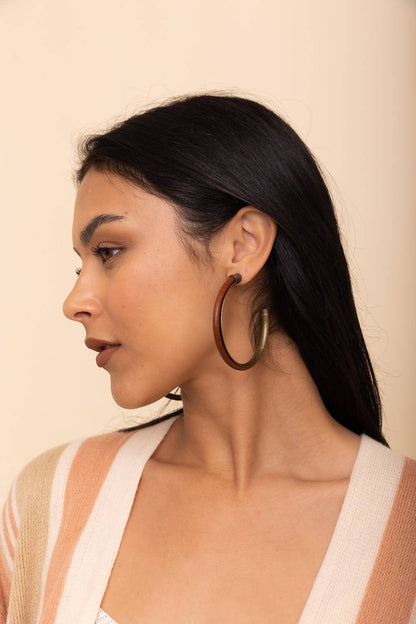 Side profile of a woman wearing bronze hoop earrings against a beige background.