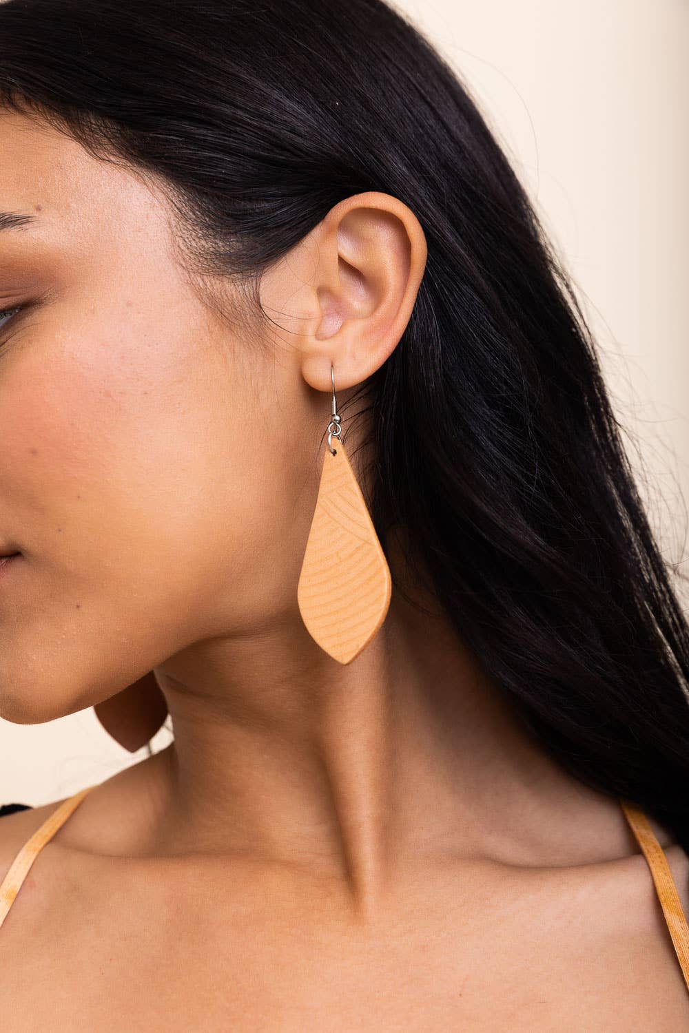 Close-up of a woman wearing a tan teardrop earring with a neutral background.