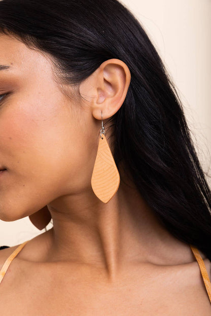 Close-up of a woman wearing a tan teardrop earring with a neutral background.