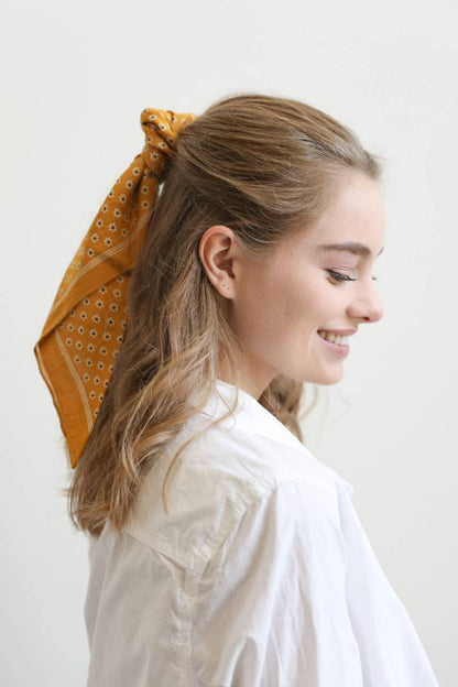 Mustard yellow patterned bandana tied in woman’s hair