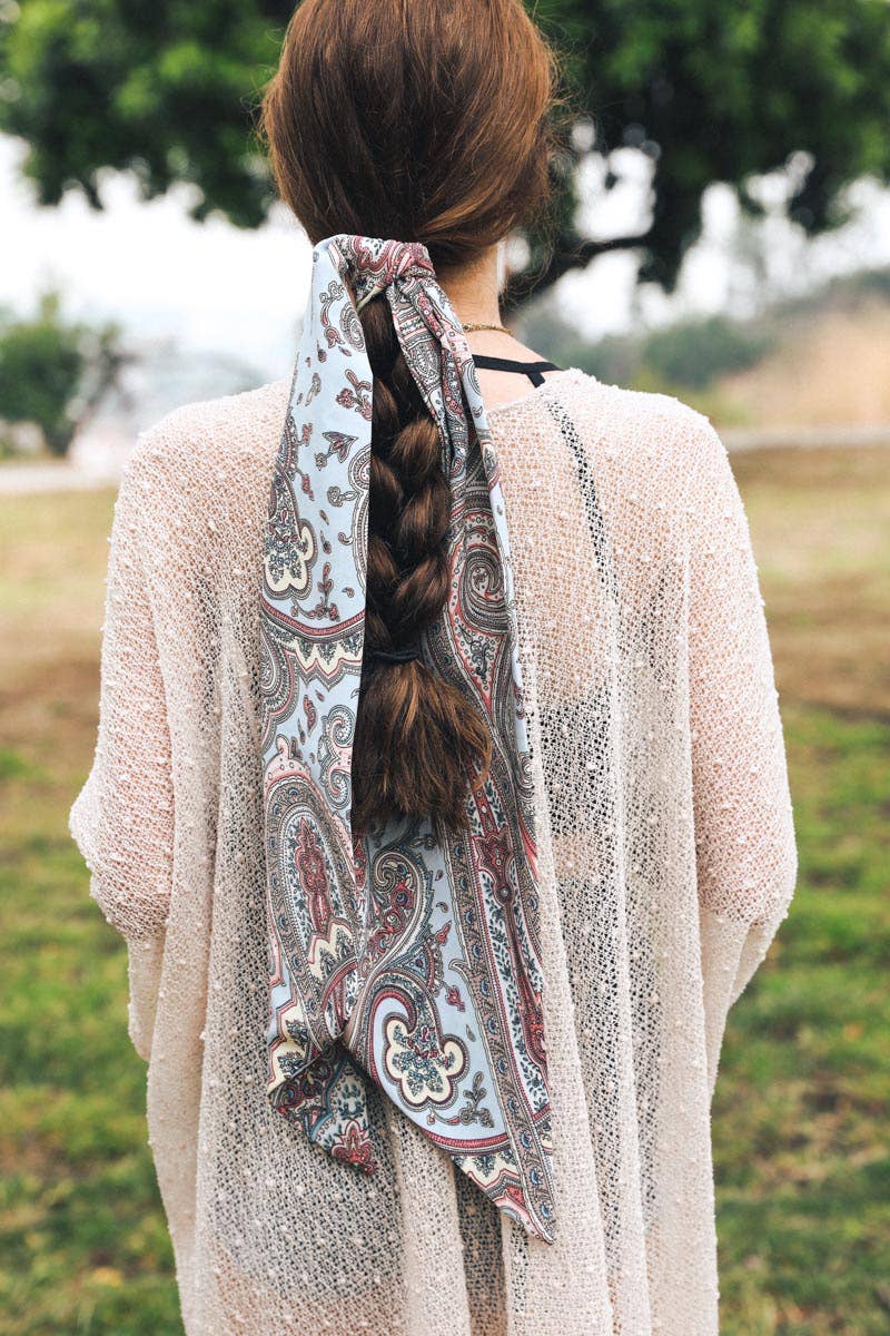 Woman with long braid wearing a blue paisley scarf tied loosely at the back outdoors