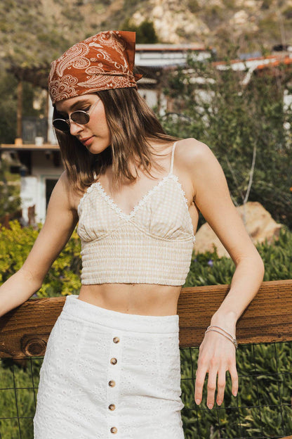 Woman in beige crop top, white pants, and rust paisley bandana headscarf outdoors