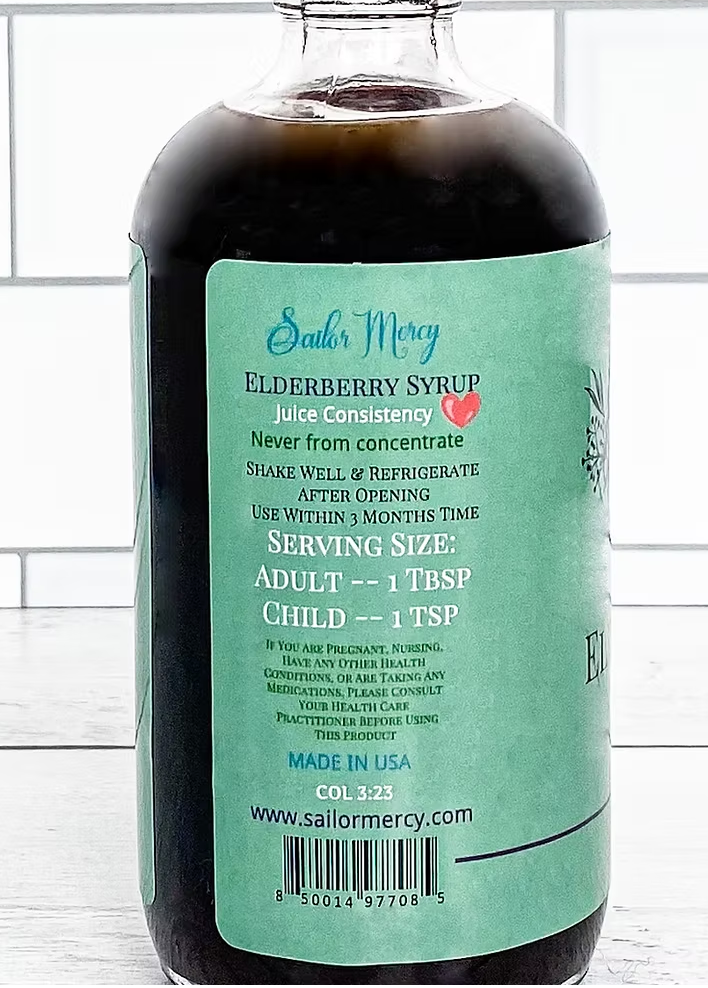 Sailor Mercy Elderberry Syrup 8 oz glass bottle back label showing serving size, nutrition details, and storage instructions on teal background.