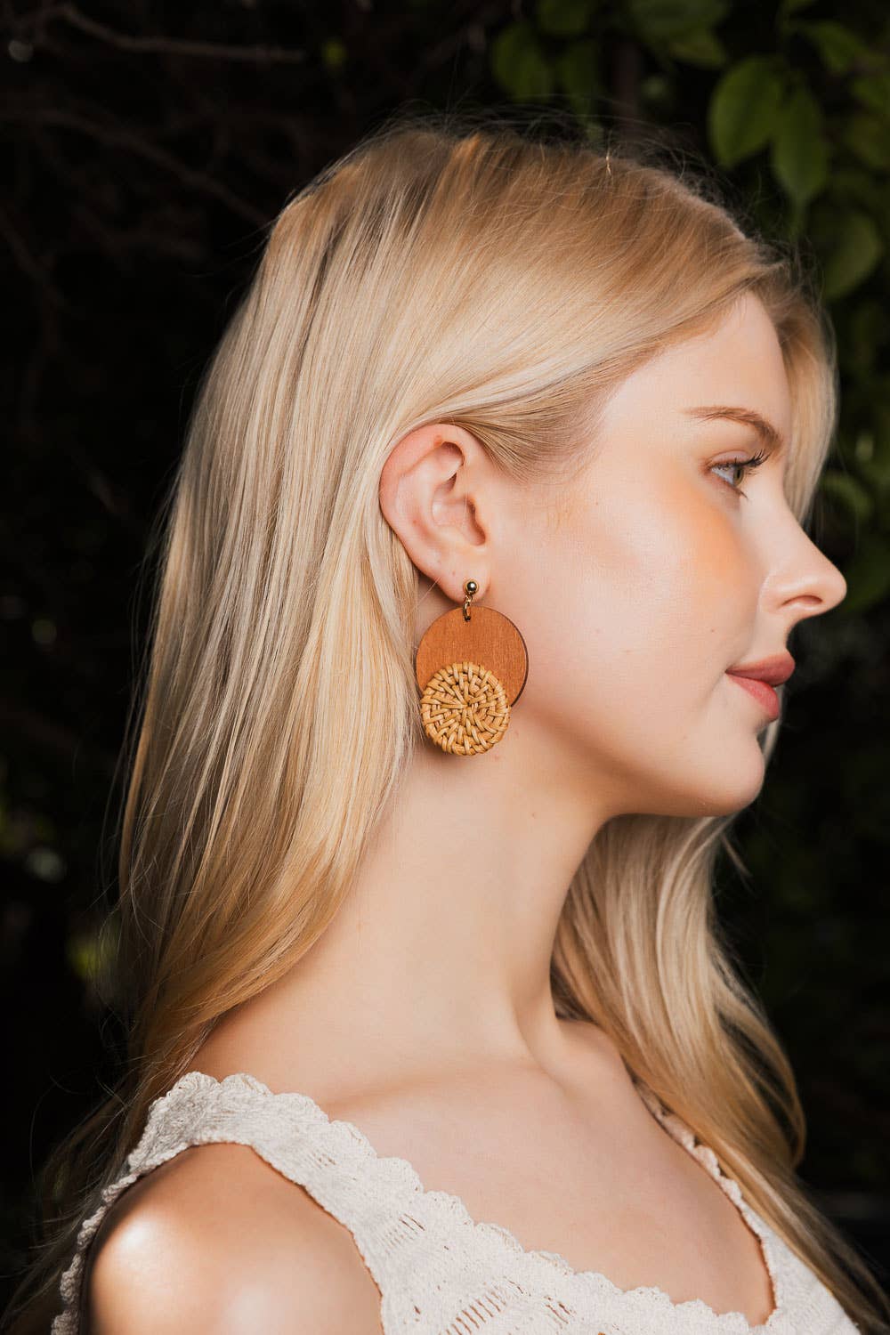 Side profile of woman wearing round wooden earrings with woven straw design