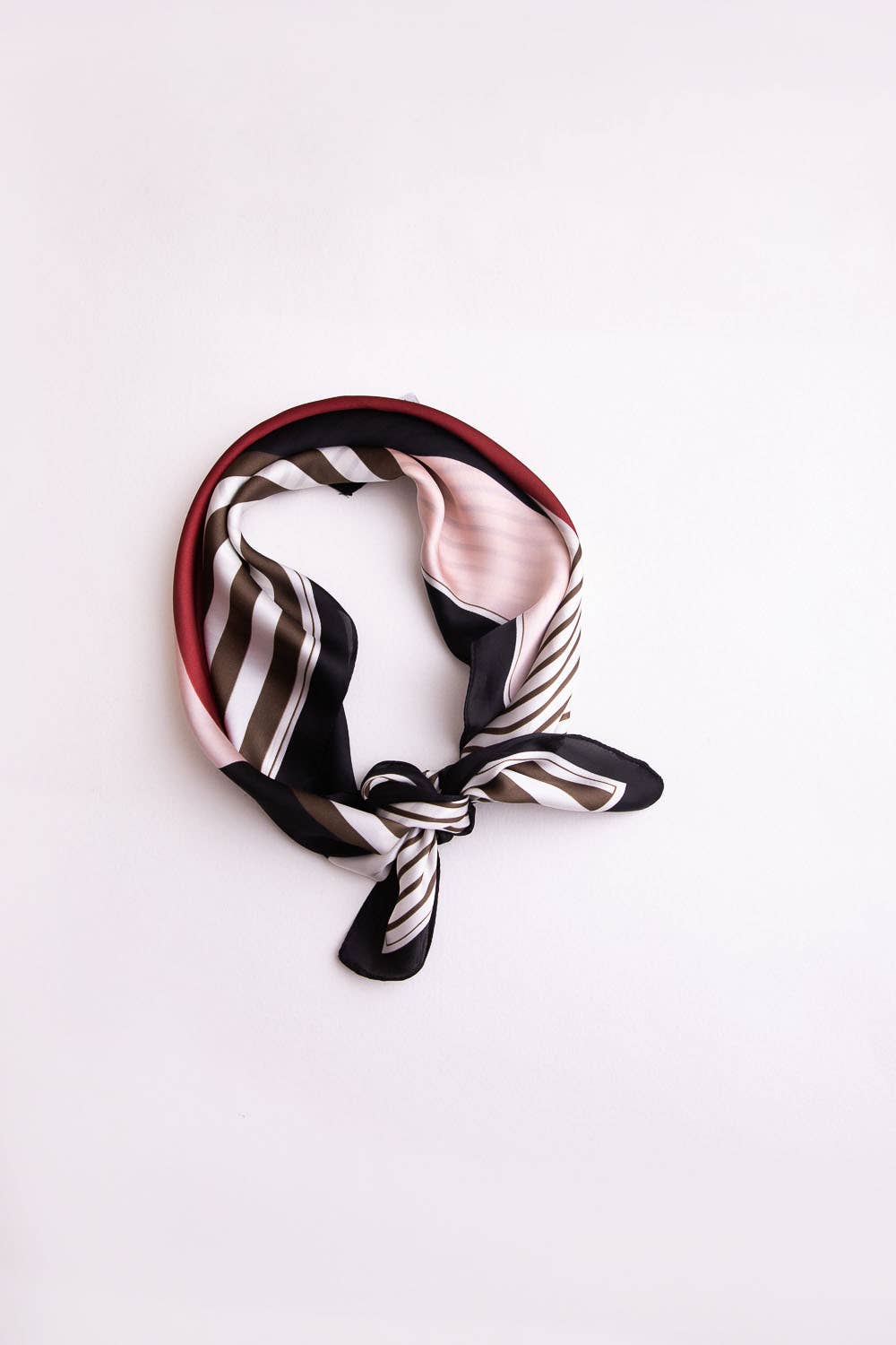 Black, white, and red striped silk scarf tied into a knot on white background