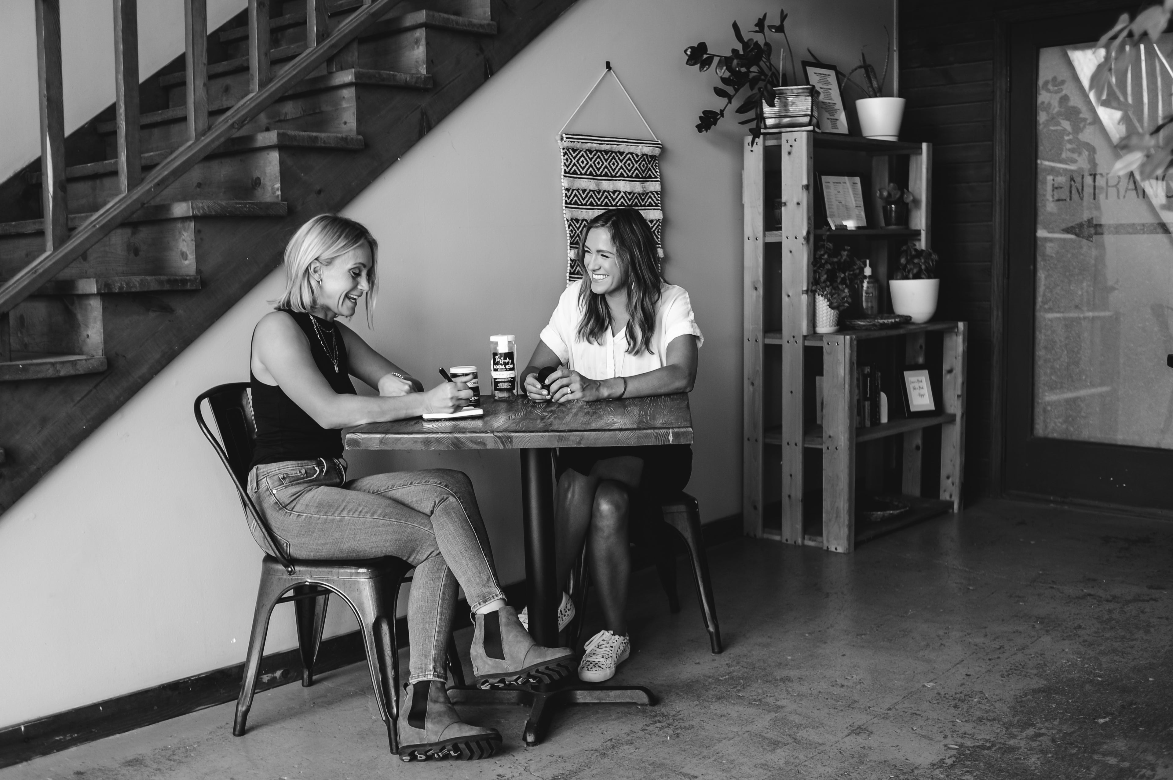 The Goodery founders sitting together at a table in a black and white photo, discussing business with juice bottle on table