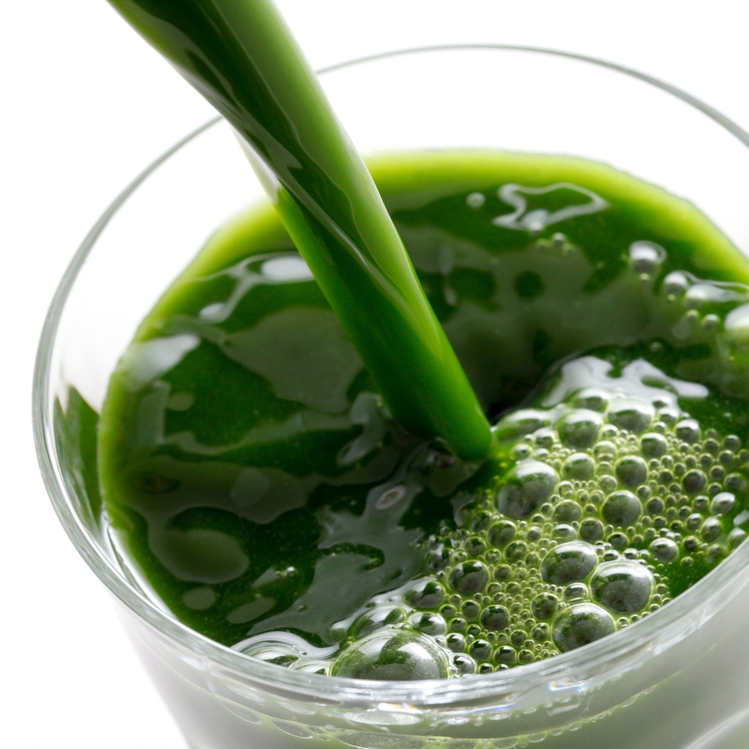 The Goodery fresh green juice being poured into a clear glass with vibrant foam and bubbles on the surface.