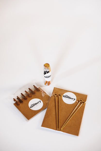The Goodery garnish kit bundle including gold cocktail picks, garnish clips, and branded packaging on a white background.