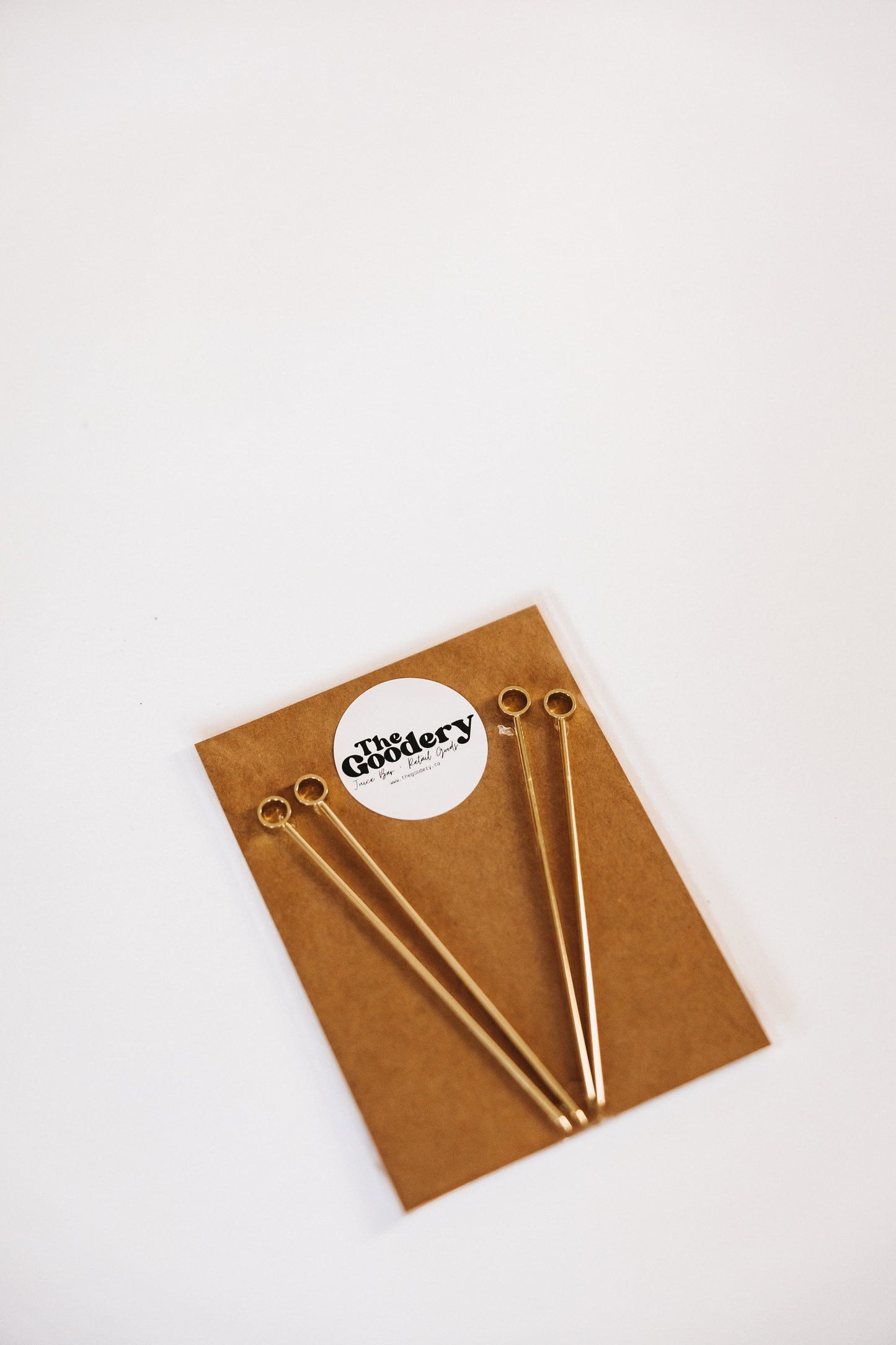 The Goodery four gold cocktail garnish picks displayed on a brown card with branded label.