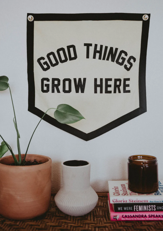 Wall banner reading Good Things Grow Here styled with houseplants, books, and candles at The Goodery