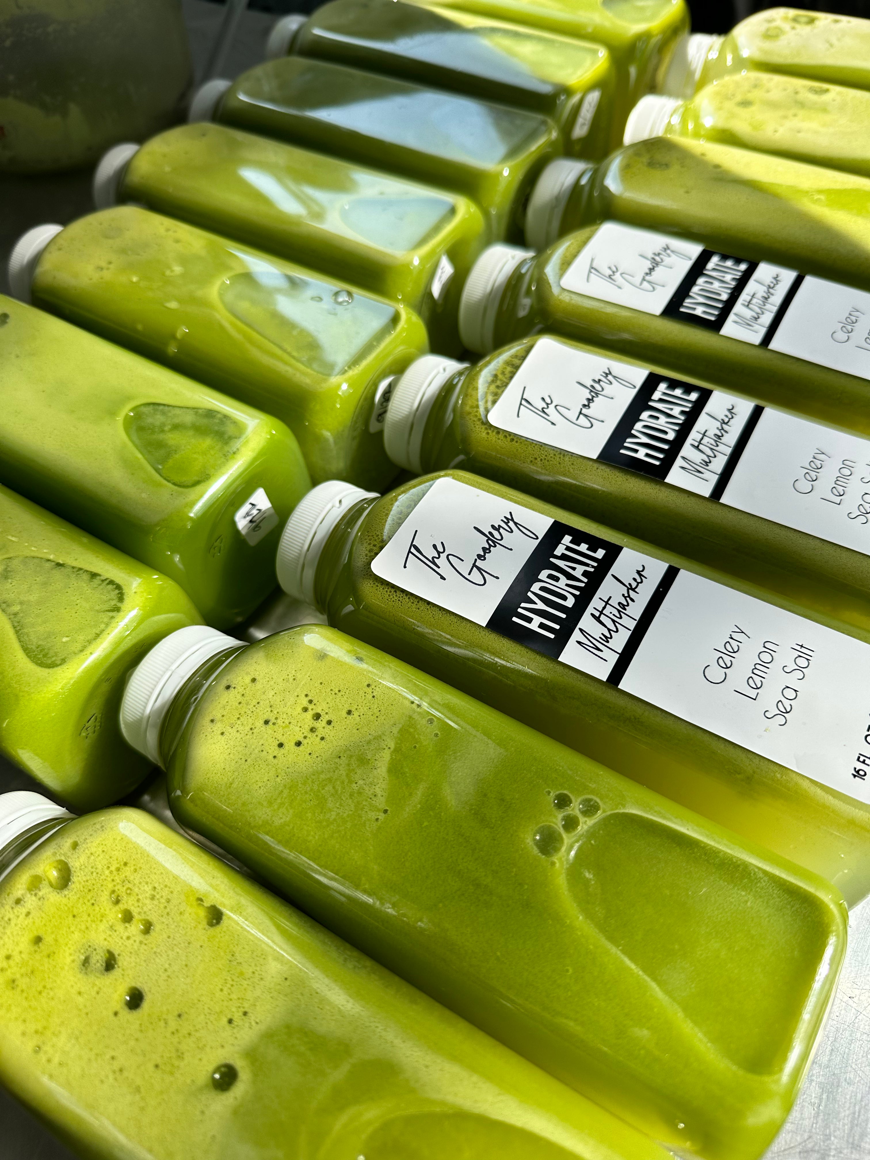 The Goodery Hydrate juice bottles labeled Celery, Lemon, and Sea Salt, arranged in rows with fresh green juice.