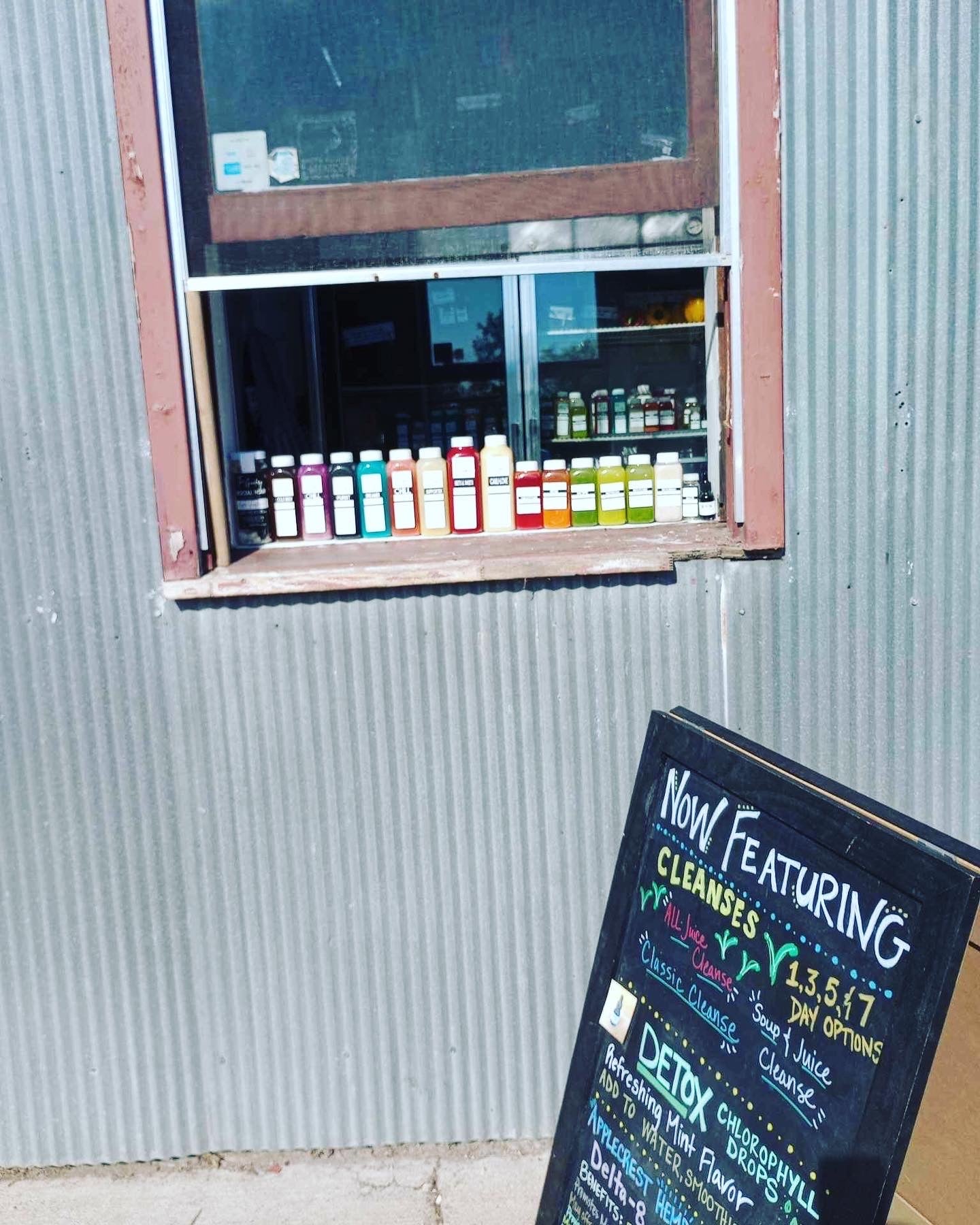 The Goodery juice bar pickup window in Stillwater with fresh bottled juices displayed and a chalkboard sign promoting juice cleanses.