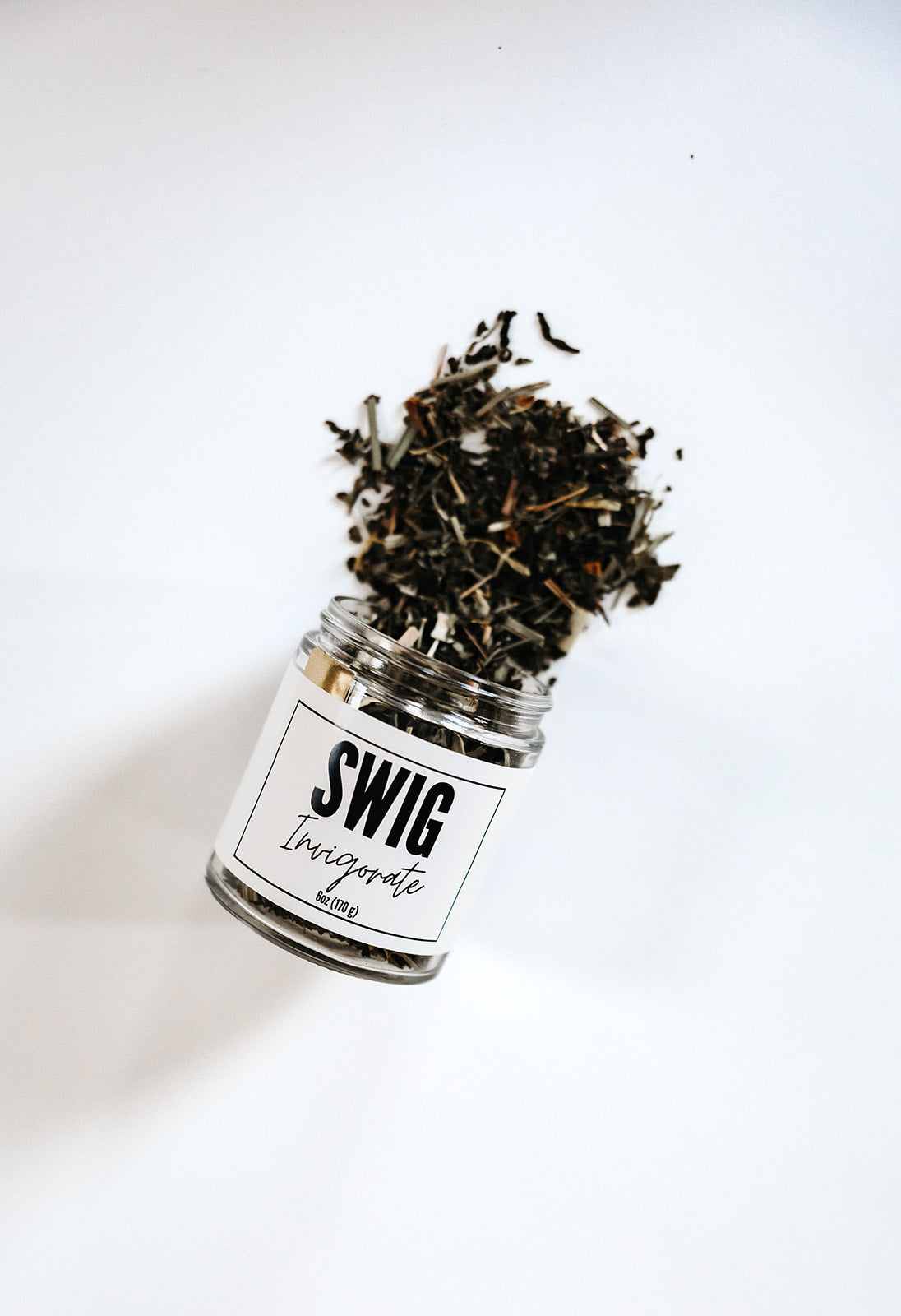 SWIG Invigorate loose leaf tea jar tipped over with herbs spilling out, product photography on white background.