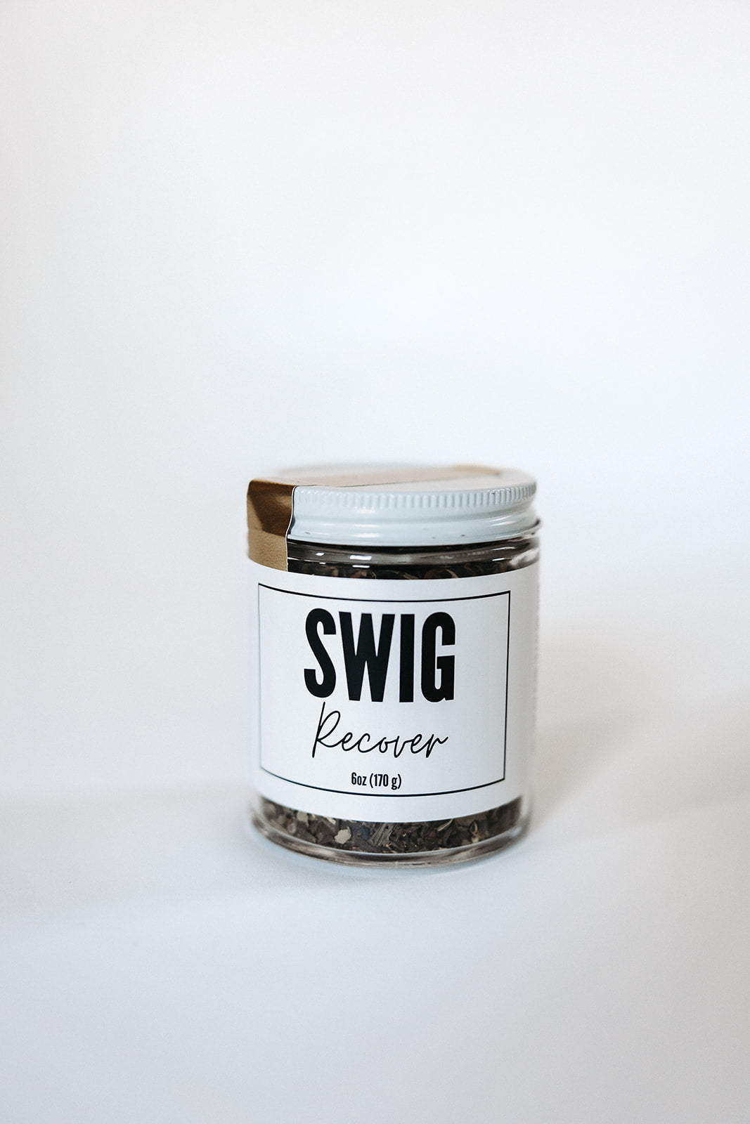Sealed glass jar of Recover tea from The Goodery Swig line, white background.