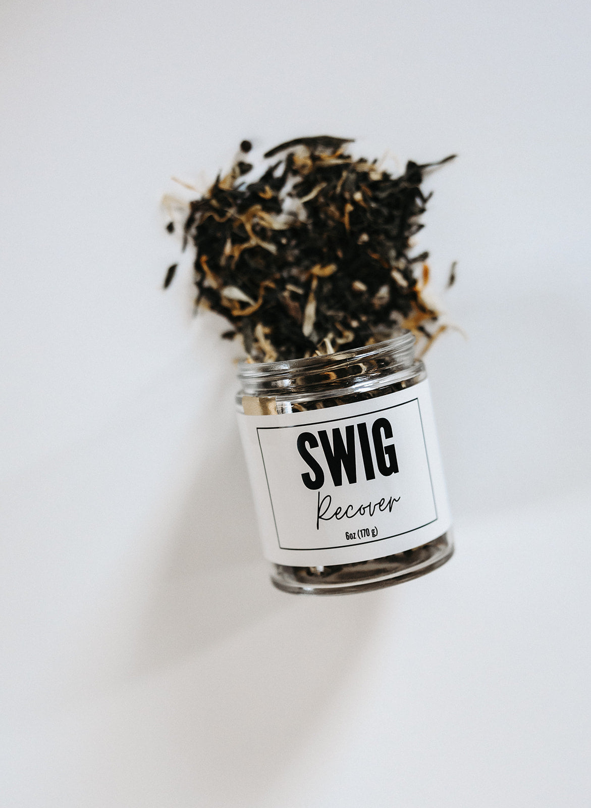 Branded jar of Recover loose leaf tea with tea leaves spilling out on white background.