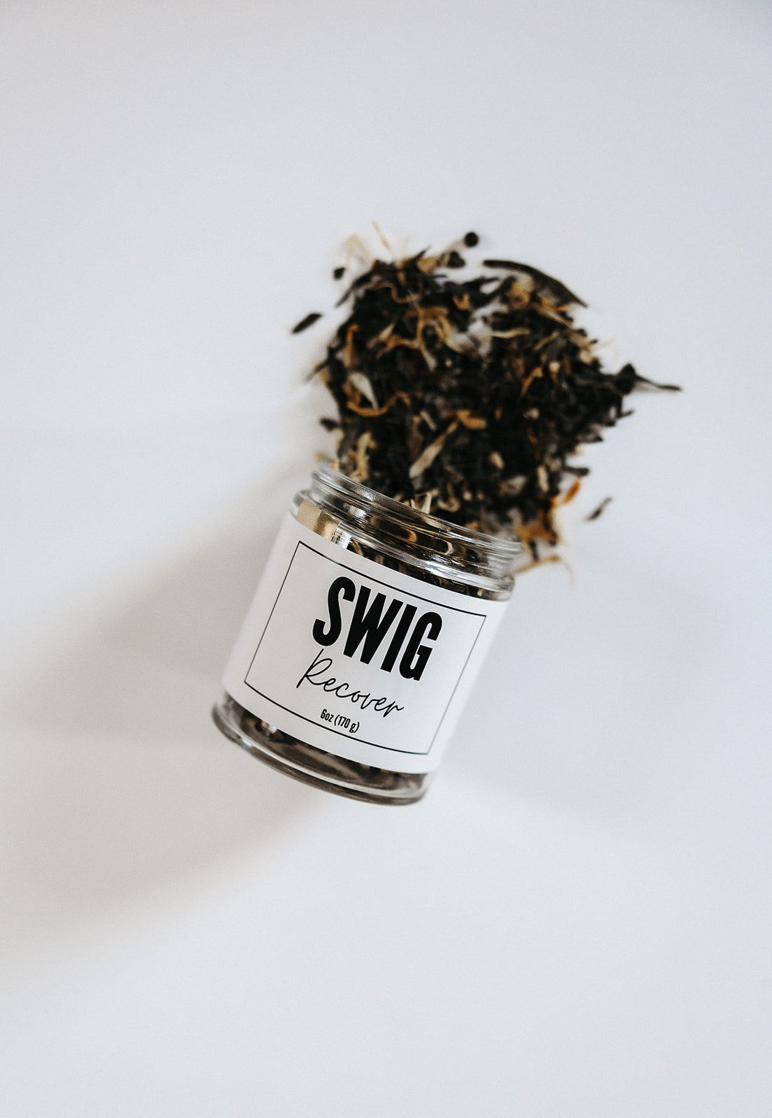 Spilled jar of Recover loose leaf tea from The Goodery Swig line, white background.