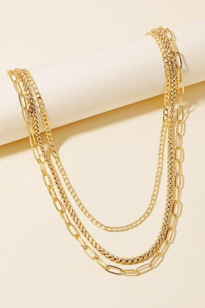 Set of three gold chain necklaces draped on a beige cylindrical display.