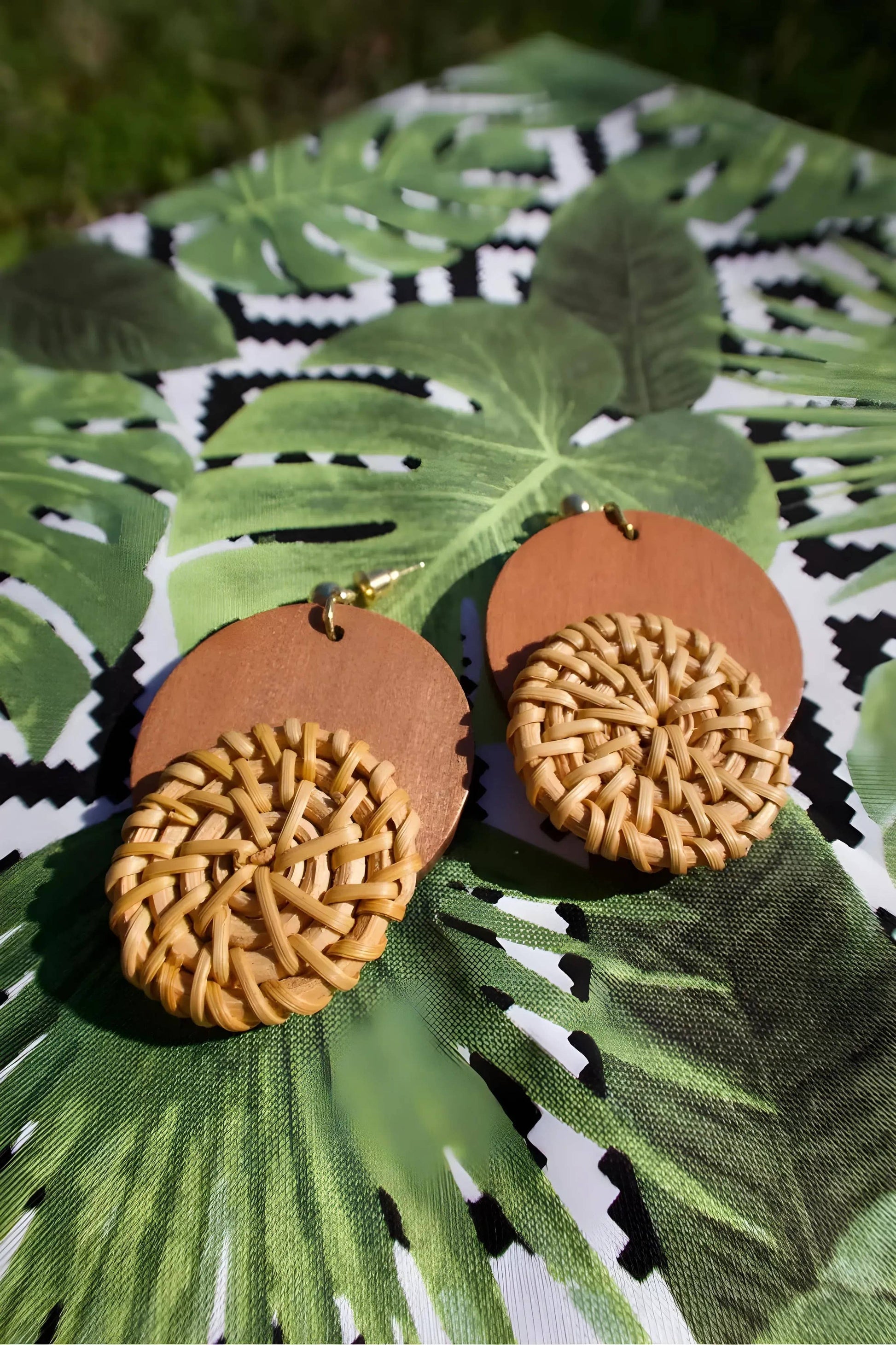 Pair of round wooden earrings with woven straw detail, displayed on leafy fabric background