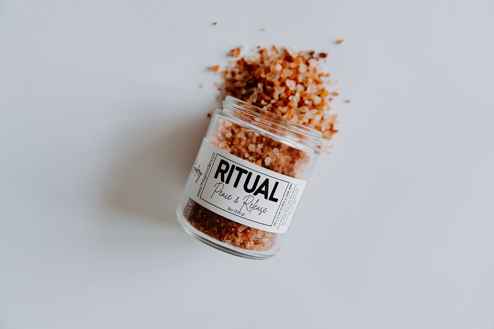 The Goodery Ritual bath soak jar labeled Peace & Relax, filled with pink mineral salts spilling onto a white background.
