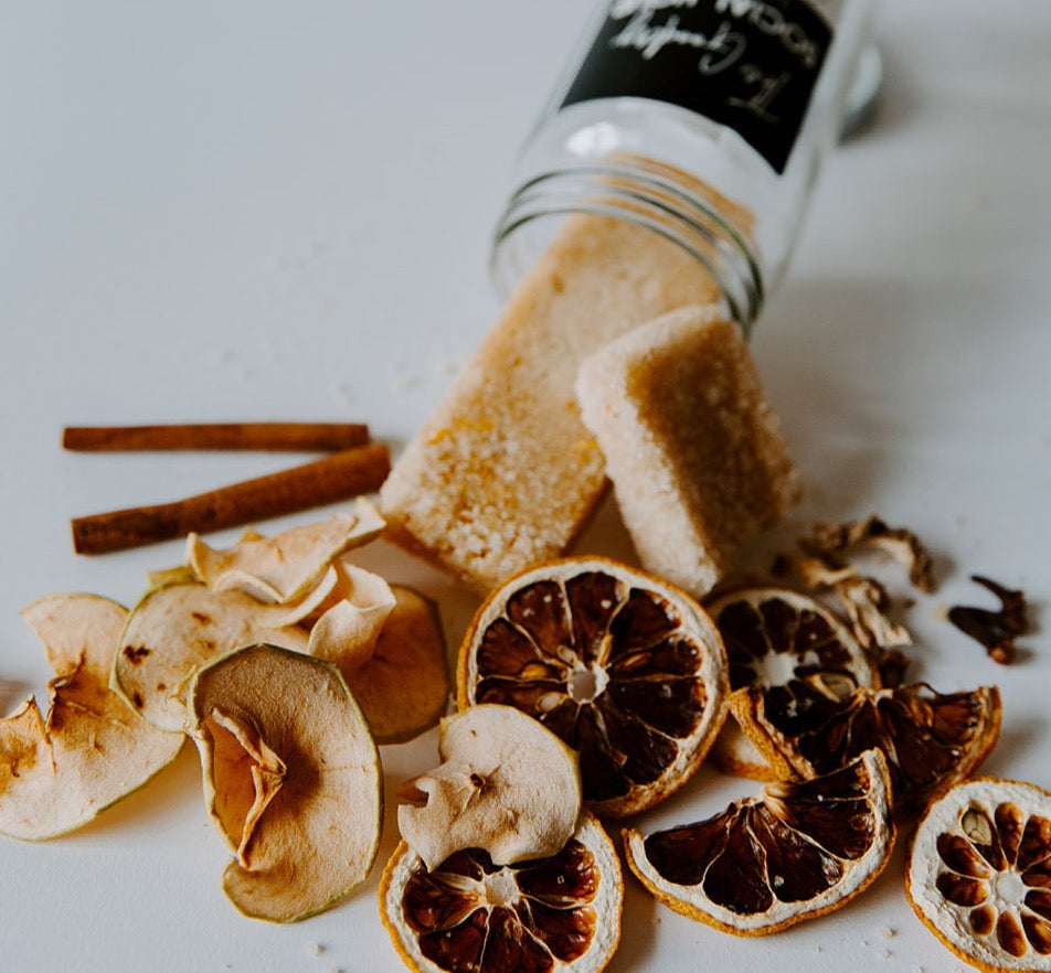 The Goodery Social Hour cocktail and mocktail infusion kit with dried apple slices, cinnamon sticks, citrus wheels, and infused sugar cubes spilling from a glass jar onto a white background.